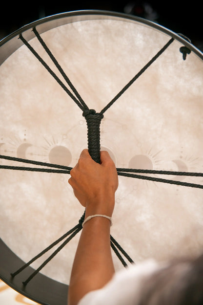 Hand holding rope of frame drum with moon phase design, energy healing instrument