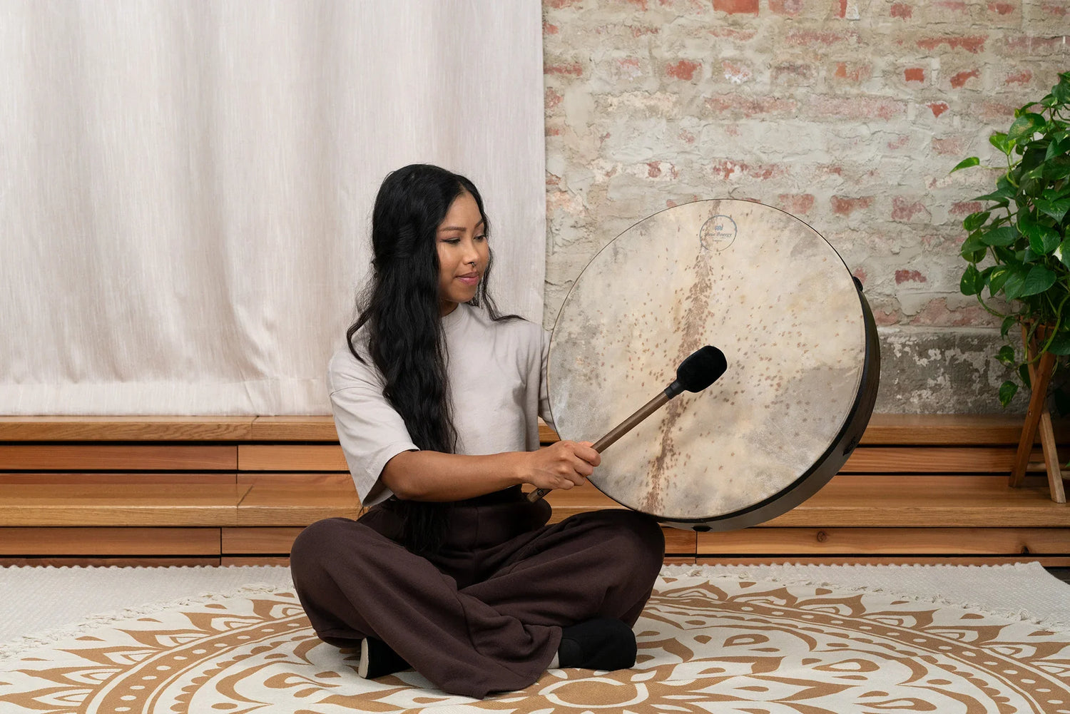 Woman playing a large frame drum for sound healing in a peaceful indoor setting