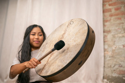 Woman playing a frame drum indoors, energy sound healing instrument