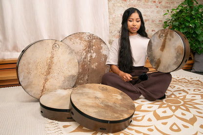 Woman playing natural frame drums for sound healing on a patterned rug indoors