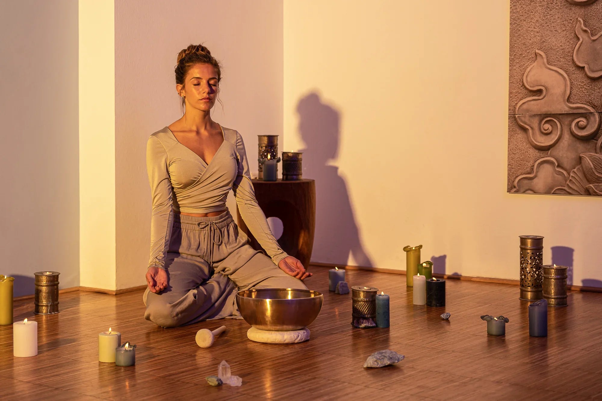 Woman meditating near a singing bowl, candles, and crystals in a peaceful healing space