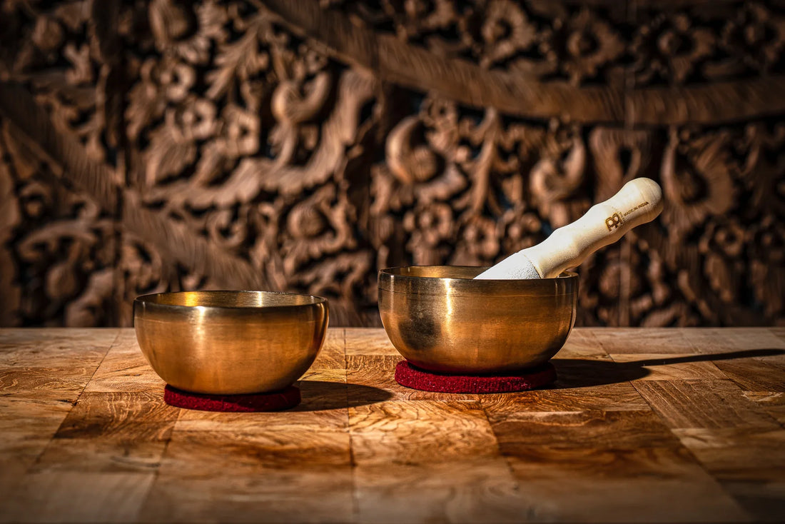 Two brass singing bowls with a mallet on a wooden table, used for sound healing