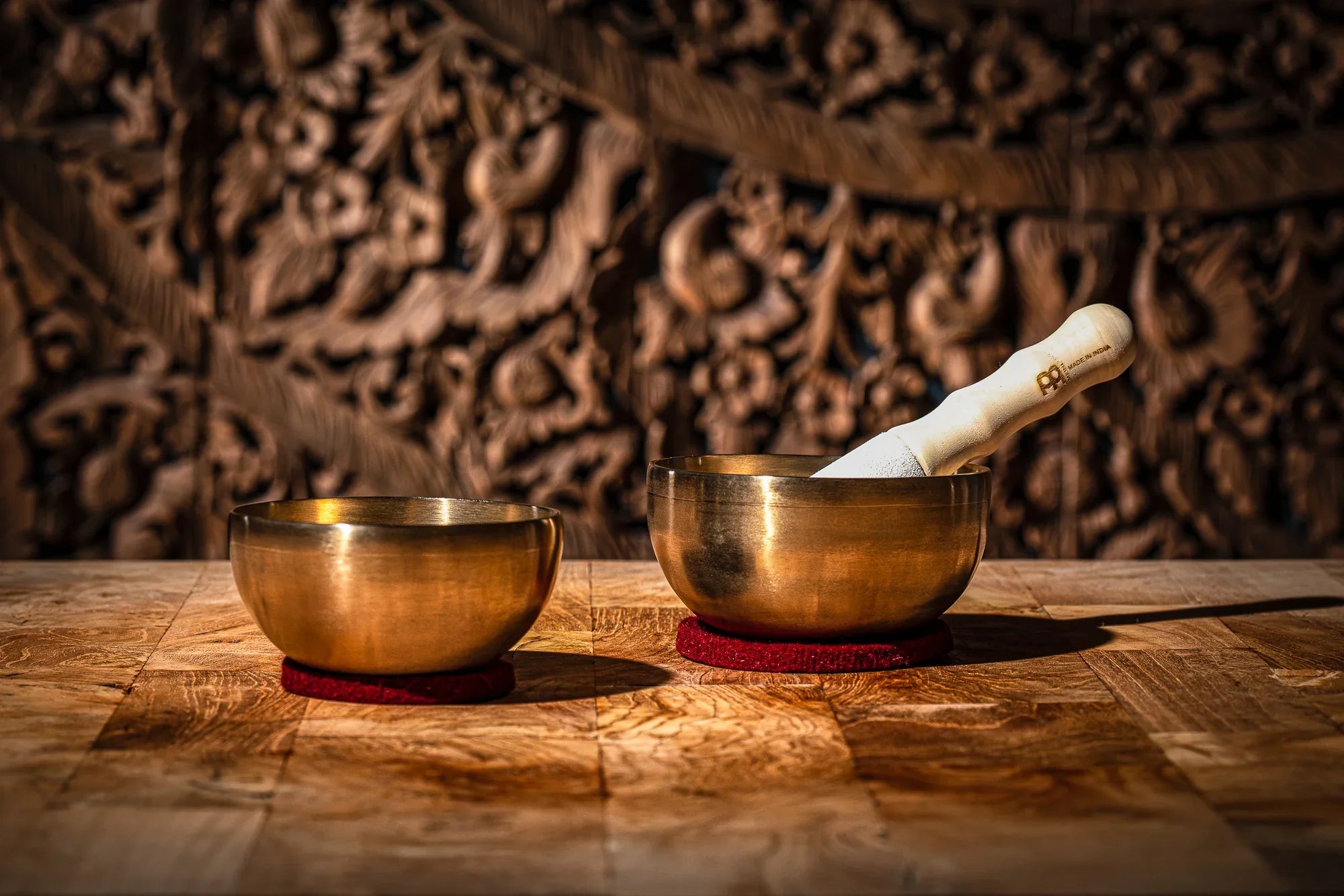 Two brass singing bowls with a mallet on a wooden table, used for sound healing