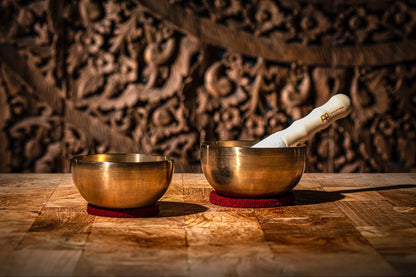 Two brass singing bowls with a mallet on a wooden table, used for sound healing