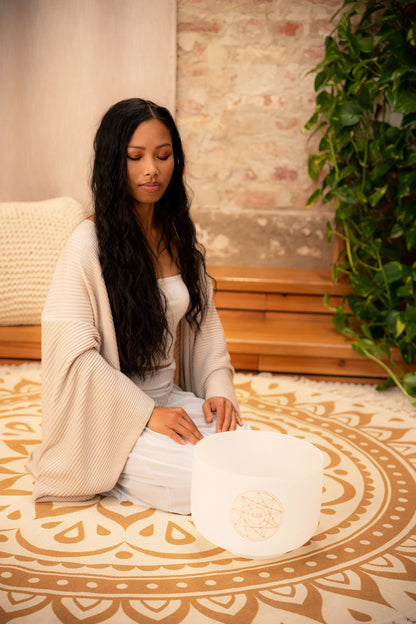 Woman meditating with frosted crystal singing bowl on patterned mat, for sound healing