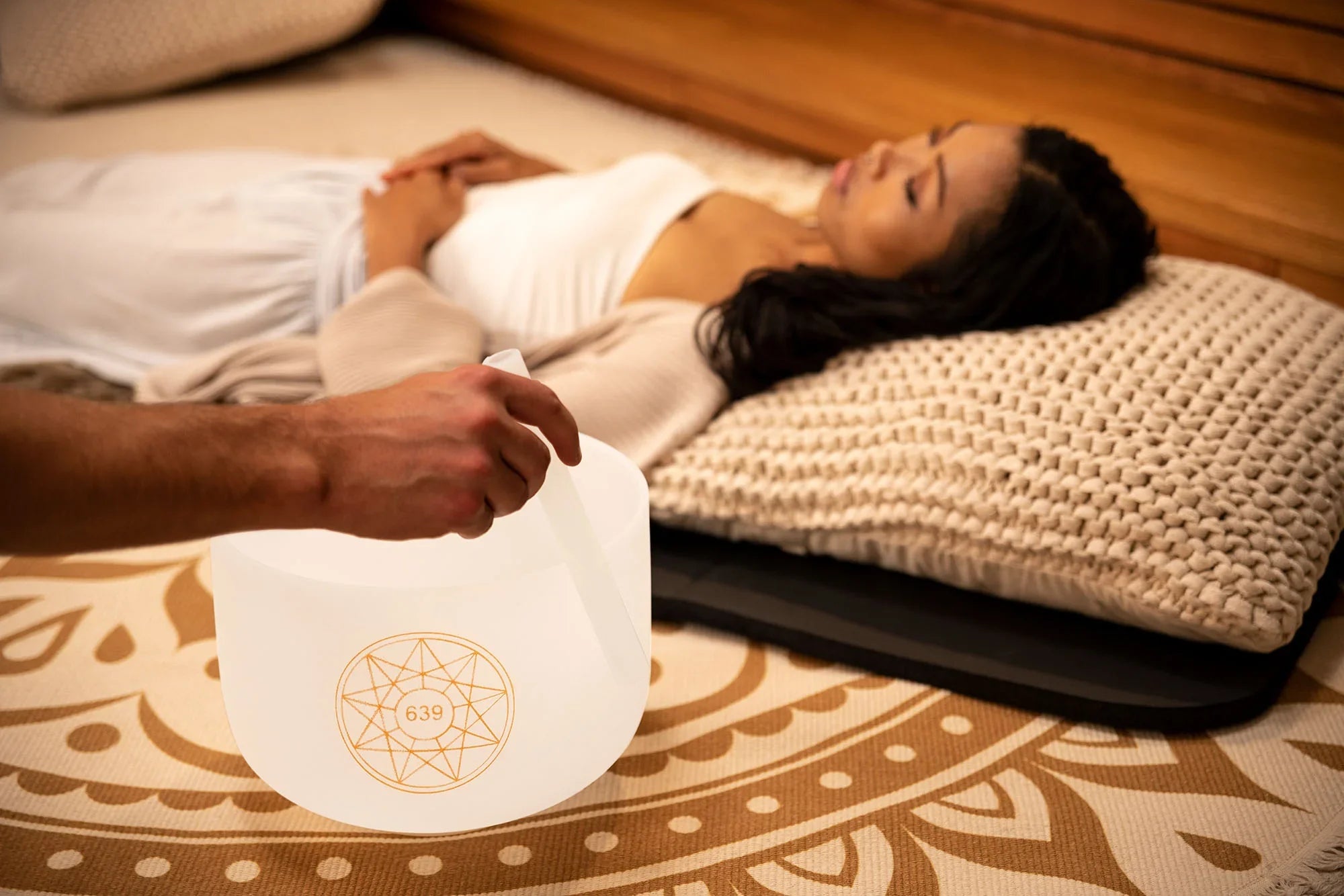 Sound healing session with crystal singing bowl near relaxed woman lying on pillow
