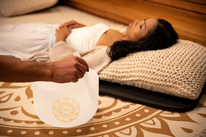 Person playing crystal singing bowl during sound healing session, woman relaxing on mat