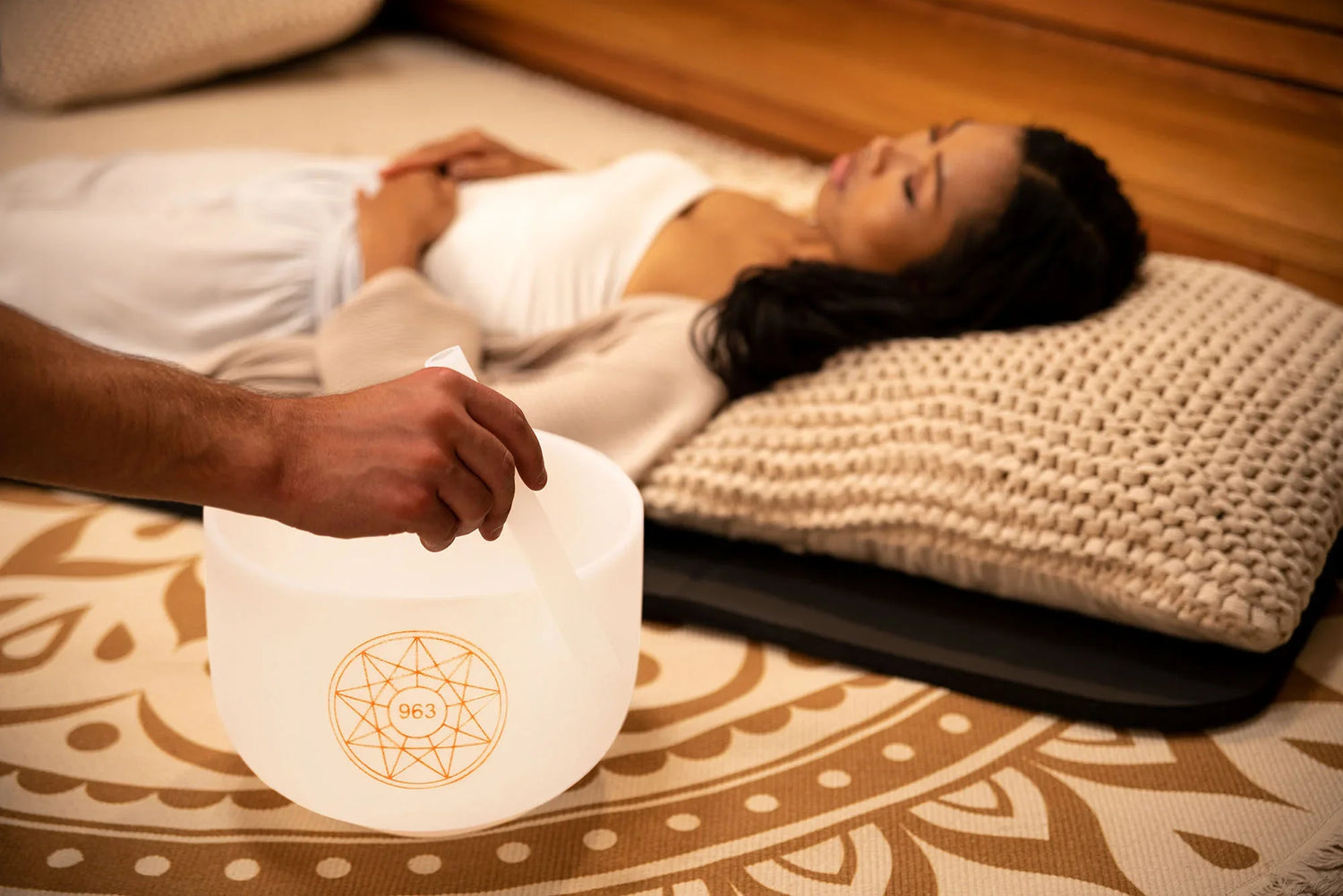 Person holding crystal singing bowl during sound healing session with woman lying on mat