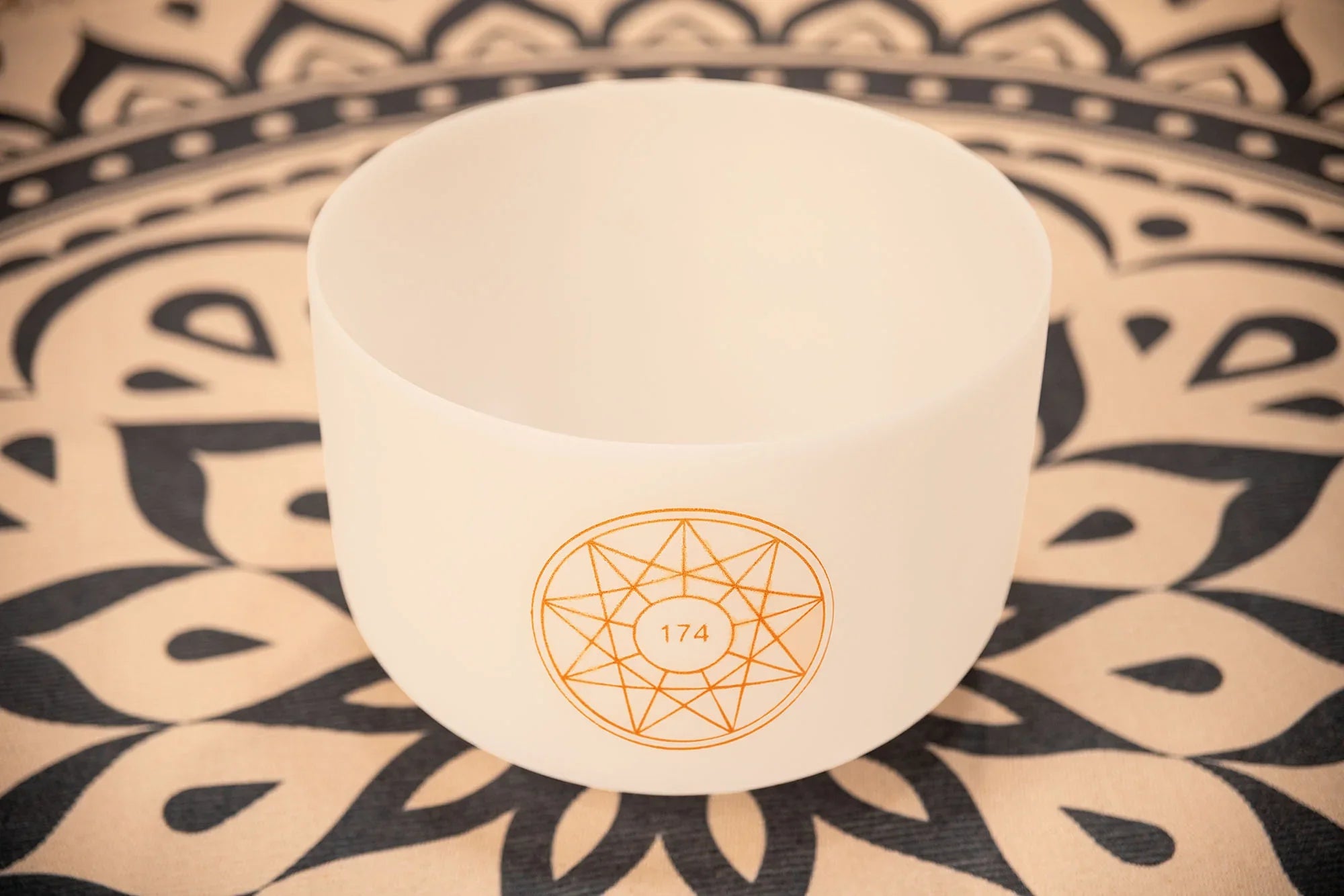 White crystal singing bowl with geometric 174 Hz design on mandala-patterned mat