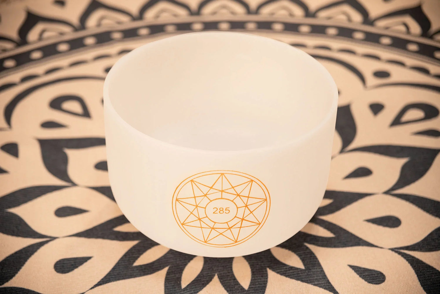 White crystal singing bowl with 285 Hz symbol on patterned mat for sound healing