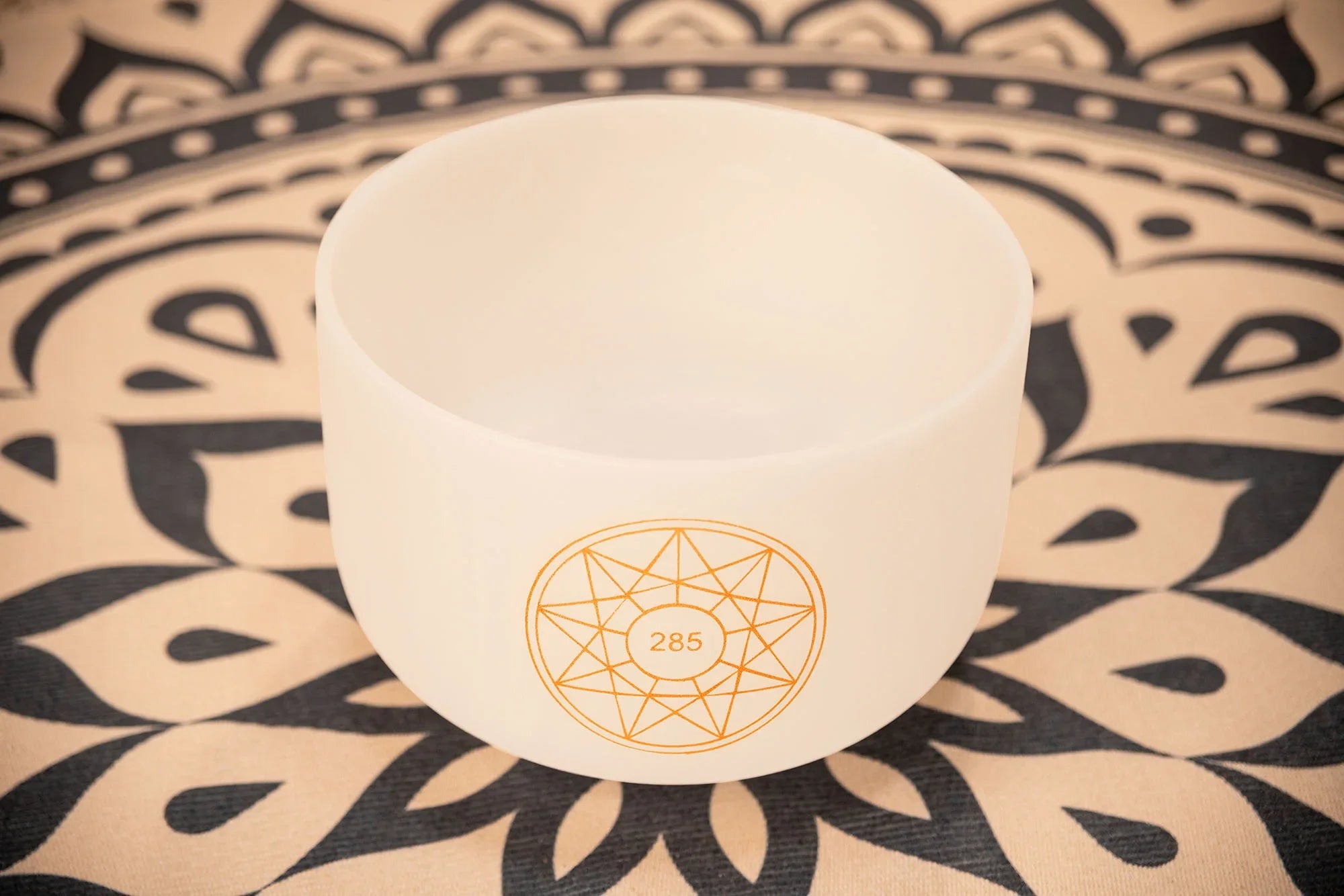 White crystal singing bowl with 285 Hz symbol on patterned mat for sound healing