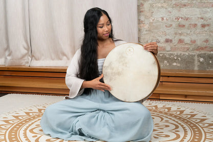 Woman holding frame drum for sound healing on decorative mat indoors