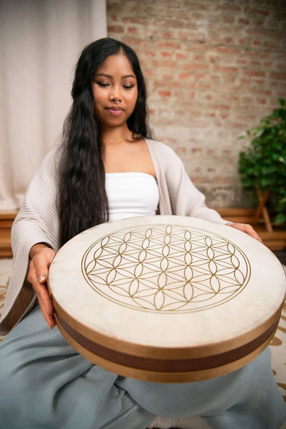Woman holding a large frame drum with geometric flower of life design in a peaceful room